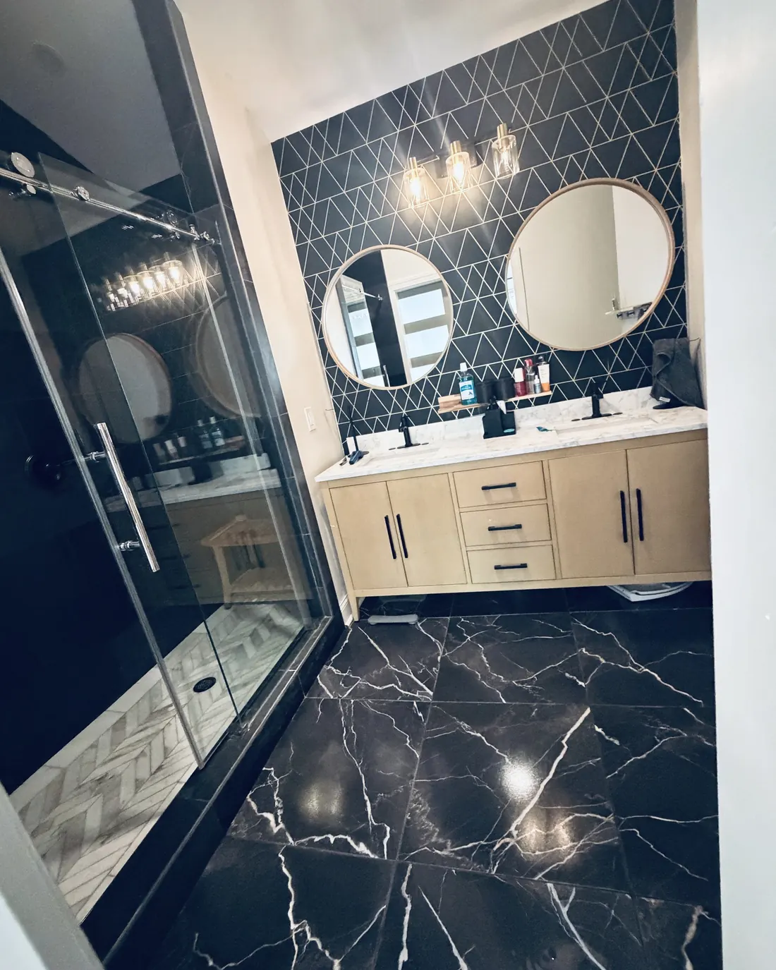 A bathroom with black marble floors, a glass shower and a double vanity, freshly cleaned