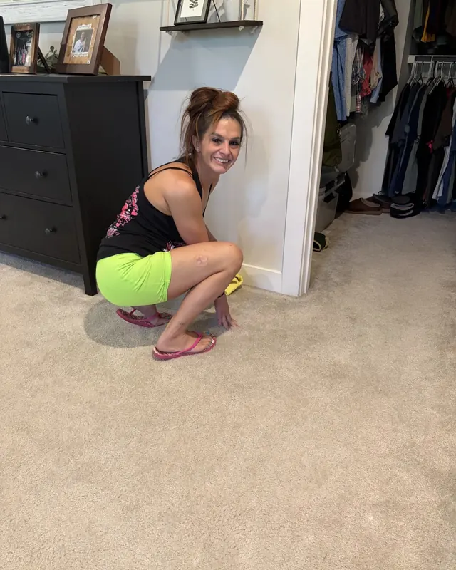 Desiree Moss, owner of Squeaky Clean, smiling while cleaning a bedroom baseboard