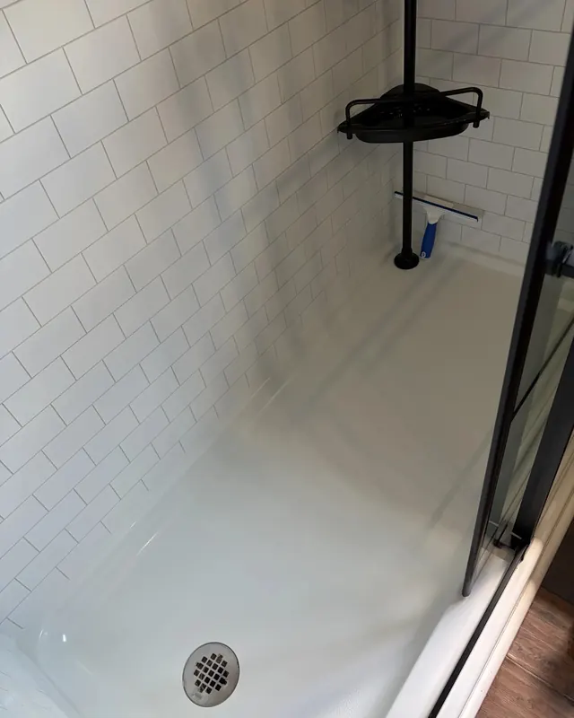A white shower pan and subway tile after a deep clean removed rust and hard water staining