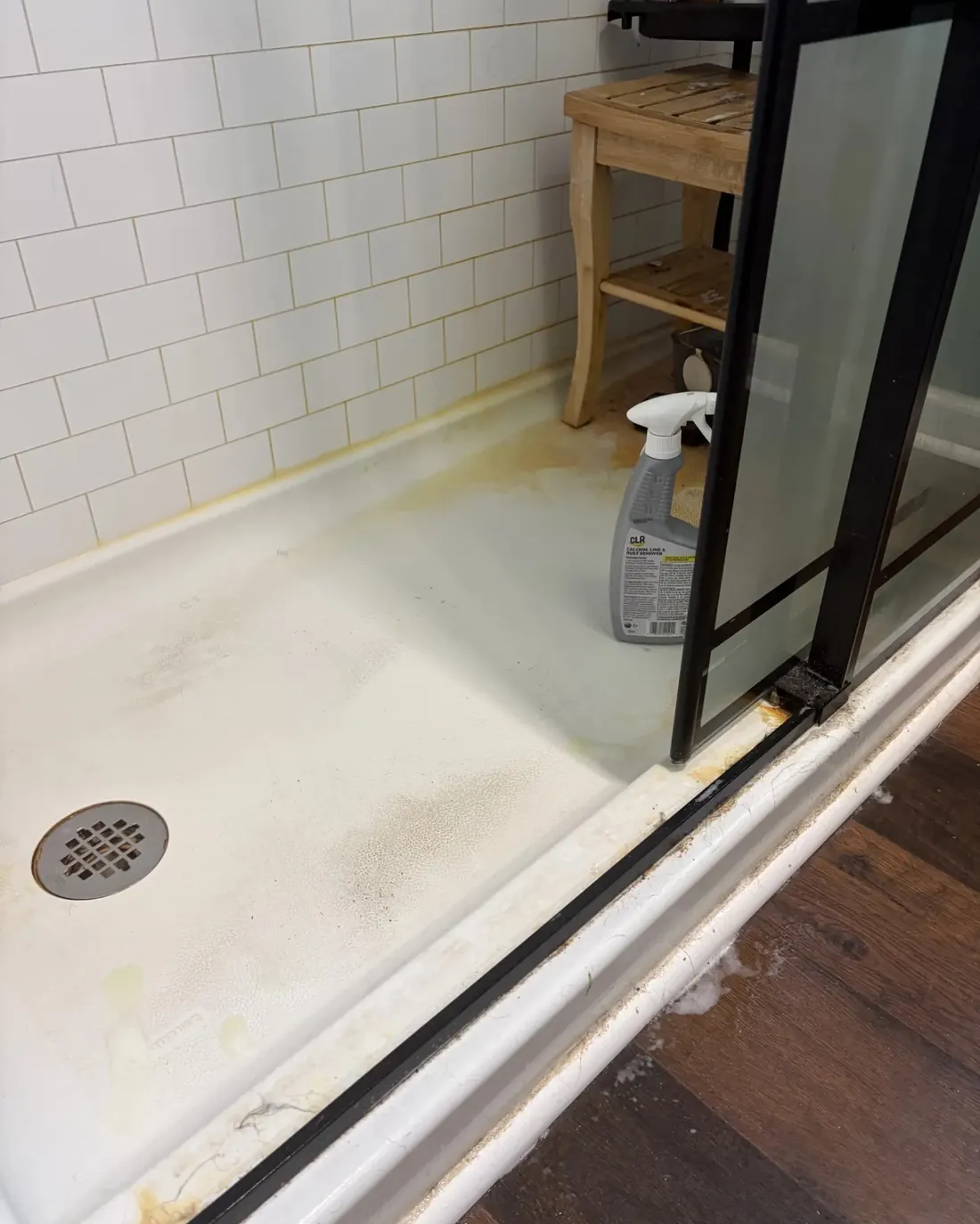 Before: shower pan with rust and hard water staining around the drain and along the door track