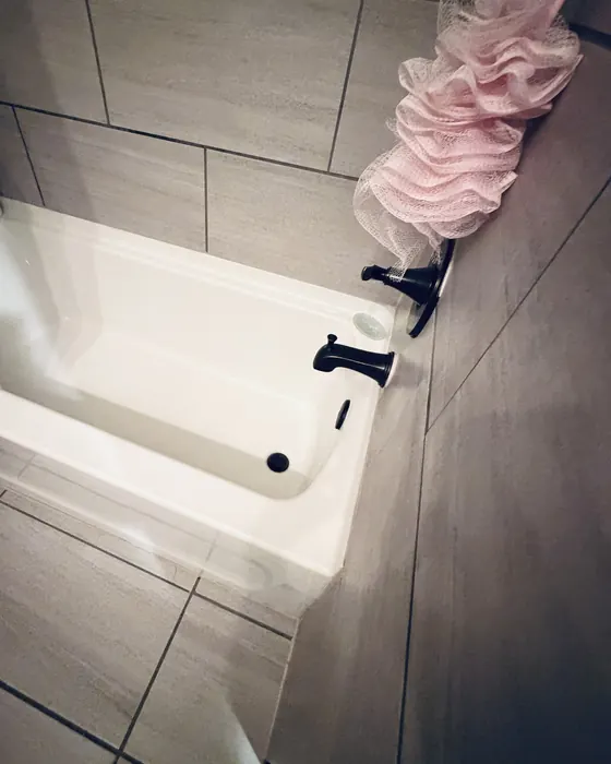A clean white bathtub with dark fixtures and gray tile